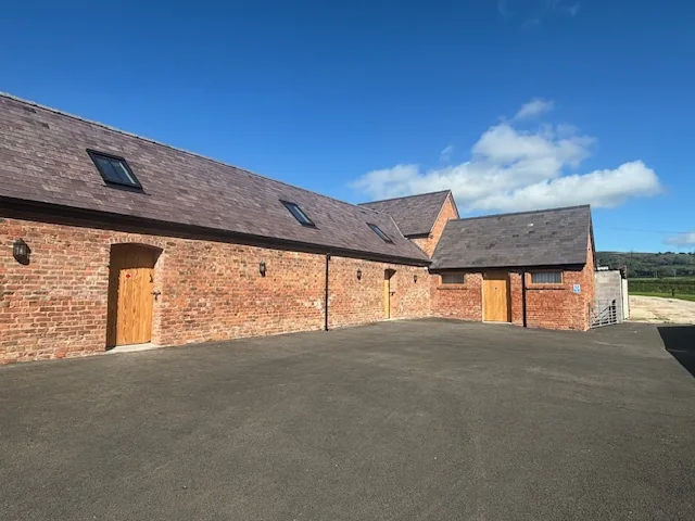 The converted red-brick barn that holds the self storage rooms, with a slate roof, rooflights and timber doors onto a tarmac forecourt.